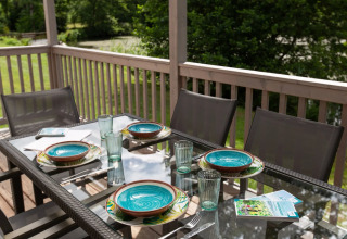 Buiteneettafel gedekt voor vier op een vakantiepark met glamping, kleurrijke borden en glazen.
