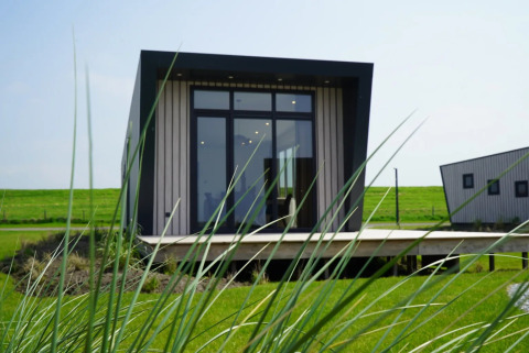 Cabaña moderna de glamping en parque vacacional, vista entre césped verde y otra cabaña al fondo.
