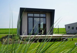 Cabaña moderna de glamping en parque vacacional, vista entre césped verde y otra cabaña al fondo.