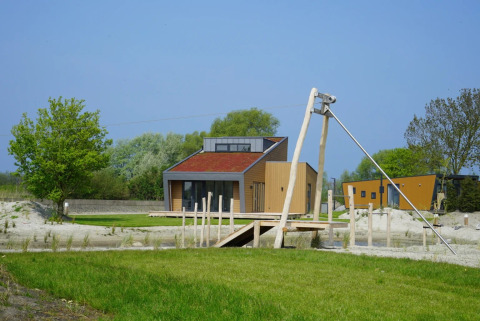 Cabaña moderna de glamping en un parque vacacional, rodeada de césped verde, árboles y cielo despejado.