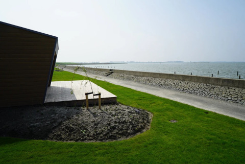 Uitzicht vanaf een vakantiepark glampingplek met groen gras, houten terras en zee op de achtergrond.