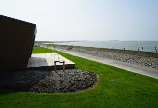 Zicht vanuit een vakantiepark-glamping met groen gras, houten terras en zee op de achtergrond.