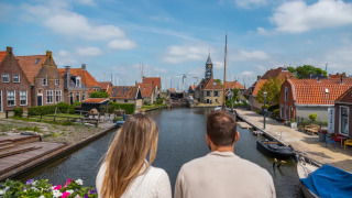 Un couple observe un canal dans un parc de vacances avec glamping, maisons colorées et bateaux autour.