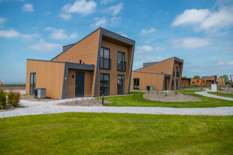 Moderne glampingaccommodaties op een vakantiepark met groene gazons en houten chalets onder blauwe lucht.
