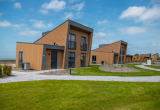 Modern glamping cabins at a holiday park with green lawns, contemporary wooden design and blue sky.