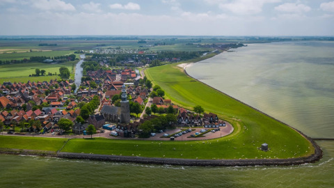Luchtfoto van een vakantiepark met glampingaccommodaties aan de kust, omgeven door velden en dorp.