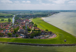 Aerial view of a holiday park with glamping accommodations on the coast, surrounded by fields and a village.