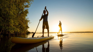 Deux personnes font du paddle sur un lac au coucher du soleil près des arbres, séjour glamping en nature.