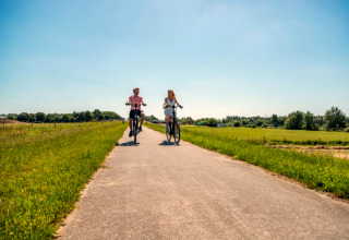 Deux personnes font du vélo sur un chemin ensoleillé, entourées de verdure dans un parc de glamping.