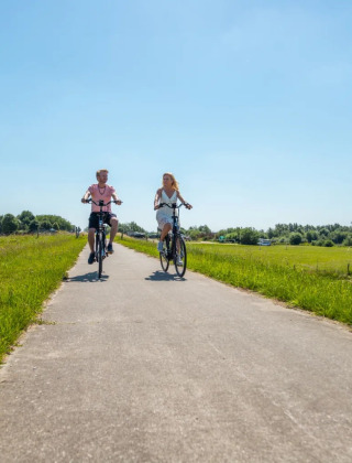 Deux personnes font du vélo sur un chemin ensoleillé, entourées de verdure dans un parc de glamping.