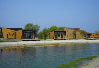 Moderne huisjes aan het water in een vakantiepark met glamping accommodaties, omringd door groen.