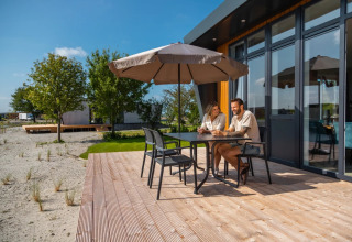 Pareja relajándose en terraza de madera bajo sombrilla en alojamiento glamping de parque vacacional.