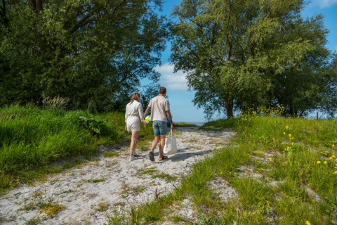 Pareja caminando por sendero arenoso entre árboles verdes en parque vacacional de glamping.