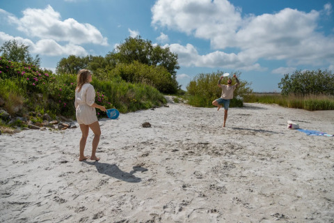 Due persone giocano a beach tennis su una spiaggia in un parco vacanze con sistemazioni glamping.