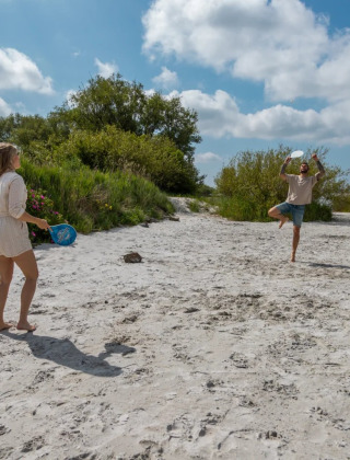 Dos personas juegan tenis de playa en un parque vacacional con alojamientos de glamping cerca de la naturaleza.