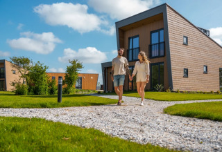 Couple walking hand in hand along a path in front of modern glamping lodges at a holiday park.