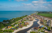 Holiday park with glamping lodges by a lake, surrounded by greenery, water, and beautiful sky.
