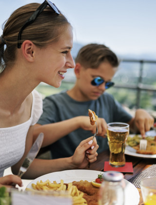 Dos jóvenes disfrutan una comida al aire libre con papas fritas y cerveza en un parque con glamping.