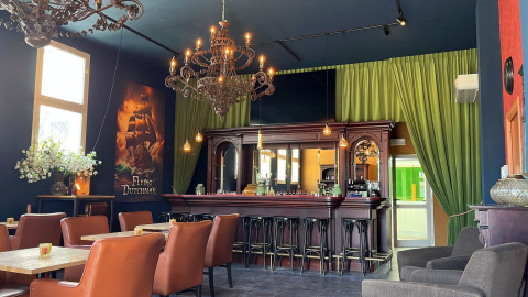 Elegante Bar mit Ledersesseln, Kronleuchtern und grünem Vorhang im Urlaubspark Per Amore del Vino, Lombardei.