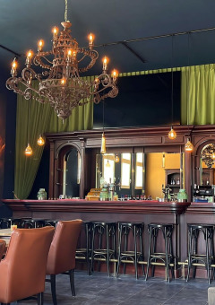 Elegante bar con candelabros, sillones de cuero y cortinas verdes en Per Amore del Vino, Lombardía, Italia.