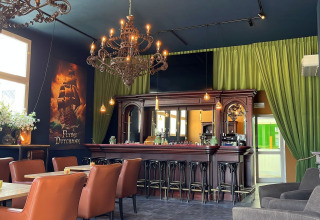 Chic bar with chandeliers, leather seating, and green curtains at Per Amore del Vino holiday park, Lombardy, Italy.