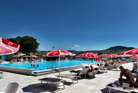 Piscina al aire libre cerca de Mornico Losana, Lombardía, Italia, con sombrillas rojas y vistas a las colinas.