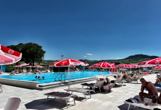 Freibad bei Mornico Losana, Lombardei, Italien, mit roten Sonnenschirmen, Liegen und Hügelpanorama.