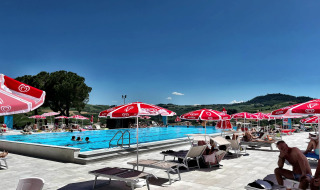 Piscina al aire libre cerca de Mornico Losana, Lombardía, Italia, con sombrillas rojas y vistas a las colinas.