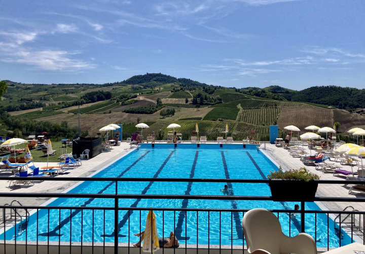 Outdoor swimming pool at Per Amore del Vino holiday park in Lombardy, Italy, with vineyard hills beyond.