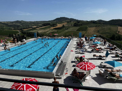 Piscina al aire libre con bañistas y sombrillas en un entorno de colinas pintorescas en Lombardía, Italia.