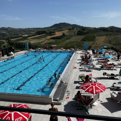 Piscina al aire libre con bañistas y sombrillas en un entorno de colinas pintorescas en Lombardía, Italia.