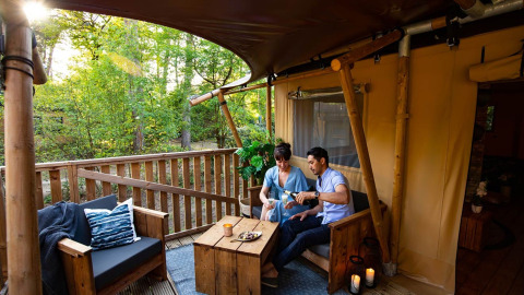 Pareja disfruta de vino en una terraza de madera, rodeada de naturaleza en Per Amore del Vino, Lombardía, Italia.