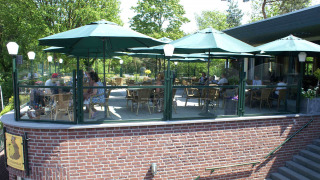 Terraza exterior con sombrillas verdes en Camping Roland, destacado parque vacacional en Limburg, Países Bajos.