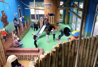 Parco giochi al coperto con bambini, scivolo e tronchi al Camping Roland, villaggio vacanze in Limburgo.
