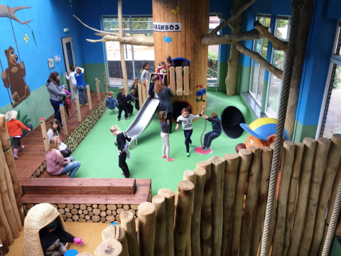Parque infantil interior con niños, tobogán y troncos en Camping Roland, un parque vacacional en Limburg.
