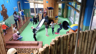 Parque infantil interior con niños, tobogán y troncos en Camping Roland, un parque vacacional en Limburg.