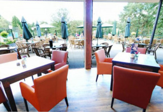 Außenterrasse eines Cafés bei Camping Roland in Limburg, Niederlande, mit bunten Stühlen und Sonnenschirmen.