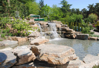 Cascata di rocce al Camping Roland, parco vacanze in Limburgo, Paesi Bassi, con abbondante vegetazione intorno.