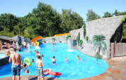 Børn og voksne nyder en swimmingpool med rutsjebane og kunstige klipper på Camping Roland i Limburg.