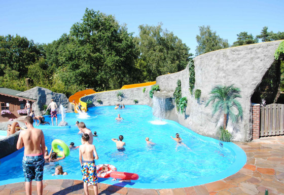 Bambini e adulti si divertono in piscina con scivolo e rocce artificiali al Camping Roland in Limburg, Paesi Bassi.