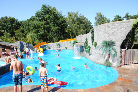 Children and adults enjoy the pool with slide and artificial rocks at Camping Roland in Limburg, Netherlands.