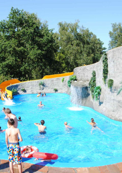 Niños y adultos disfrutan de la piscina con tobogán y rocas artificiales en Camping Roland, Limburg, Países Bajos.