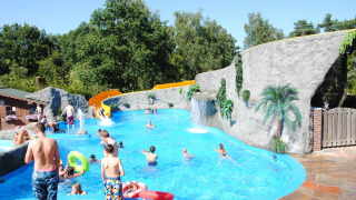 Niños y adultos disfrutan de la piscina con tobogán y rocas artificiales en Camping Roland, Limburg, Países Bajos.