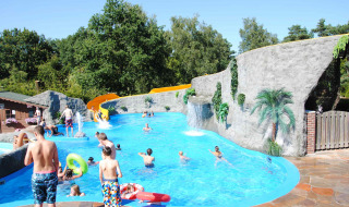 Niños y adultos disfrutan de la piscina con tobogán y rocas artificiales en Camping Roland, Limburg, Países Bajos.