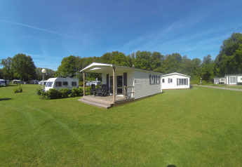 Lyst lodgehus med terrasse på grøn campingplads hos Camping Roland, Holland, omgivet af træer og natur.