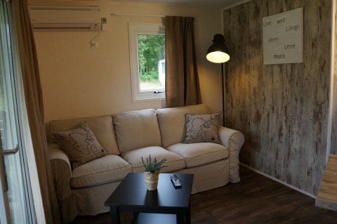 Gezellige zithoek in Lodge bij Camping Roland, Nederland, met bank, tafeltje en decoratie.
