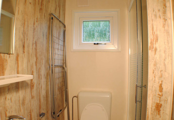 Schmales Badezimmer in einer Lodge bei Camping Roland in den Niederlanden mit WC, Waschbecken und Dusche.