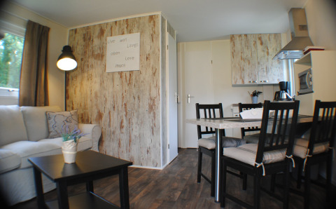Interior de un acogedor lodge en Camping Roland, Países Bajos, con sofá, mesa de comedor y pequeña cocina.
