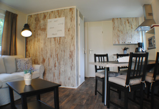 Interior de un acogedor lodge en Camping Roland, Países Bajos, con sofá, mesa de comedor y pequeña cocina.