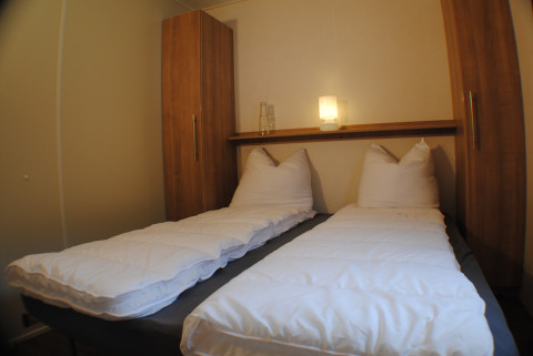 Dos camas individuales con ropa de cama blanca en una cómoda cabaña del Lodge at Camping Roland en los Países Bajos.